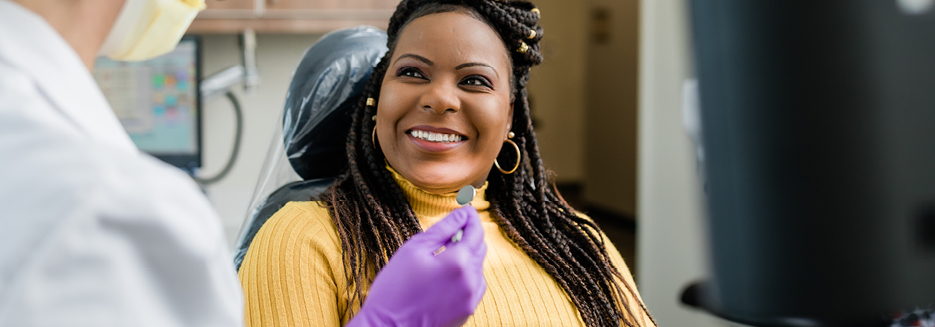 Woman in a yellow sweater smiles at the dentist during 
