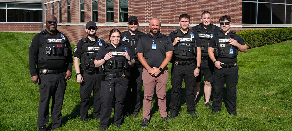 Eight of Broadlawns Public Safety officers pose in black uniforms outside of the Broadlawns Medical Center outdoor sign. 